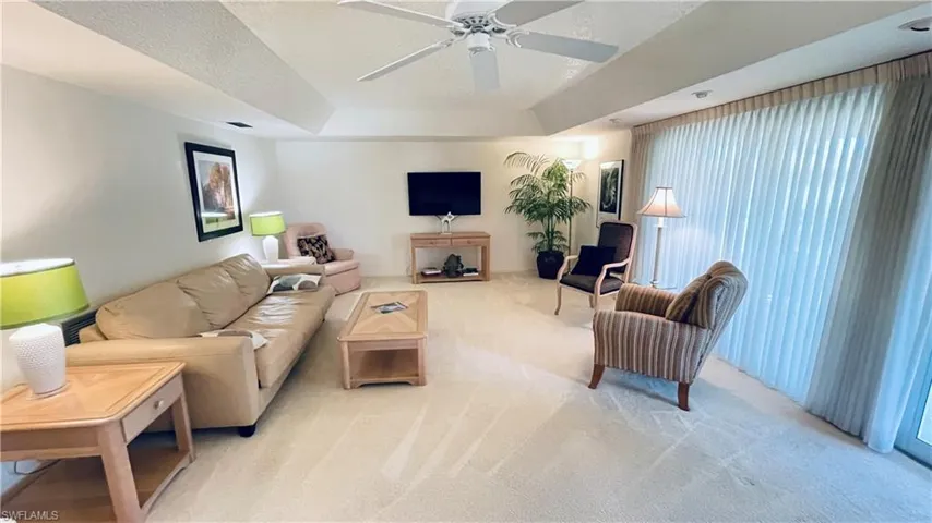 Living room with light carpet, a tray ceiling, and ceiling fan.
