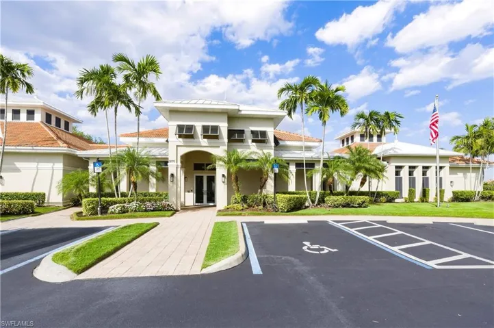 Mediterranean-style building featuring a tiled roof, stucco exterior, multiple palm trees, a paved entryway, and manicured landscaping