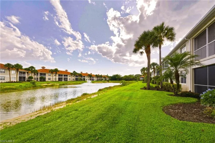 Canal-front community featuring a water fountain, mature palm trees, lush green landscaping, screened balconies, and light-colored stucco exteriors with terracotta-style roofs