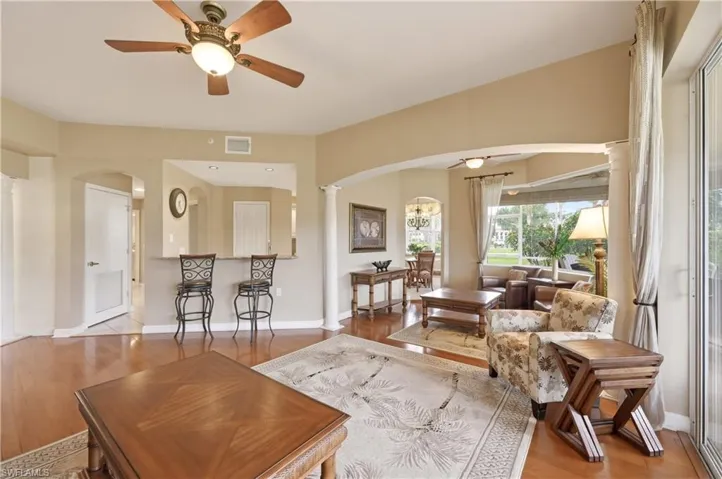 Expansive living area featuring warm wood-finish flooring, a ceiling fan with integrated lighting, and an arched entryway