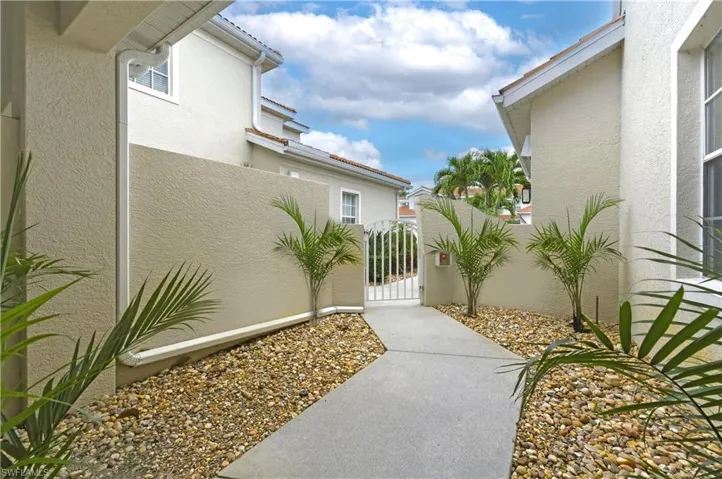 Private gated entry featuring a concrete pathway, decorative gravel landscaping, and mature palm plantings