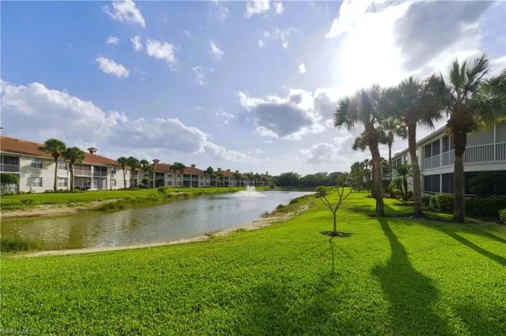 Waterfront property featuring extensive green space, mature palm trees, a prominent water feature with a fountain, and multi-story buildings with balconies