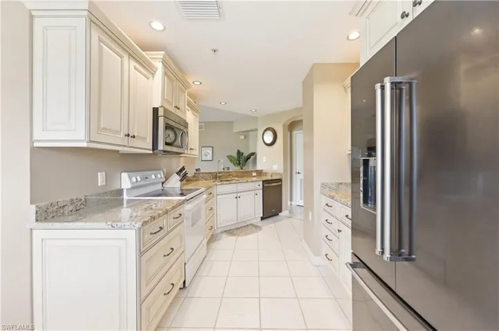 Galley kitchen featuring white cabinetry, light-toned granite countertops, stainless steel appliances, and tile flooring