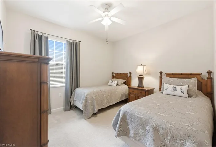 Carpeted bedroom with two wood-frame beds, a side table with a lamp, and a window with blinds and drapes