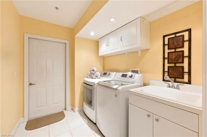 Dedicated laundry area featuring a utility sink, white base cabinetry, and upper cabinetry
