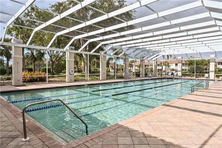 Screen-enclosed lap pool with clear water, integrated lane lines, and stainless steel grab rails, surrounded by a paver deck