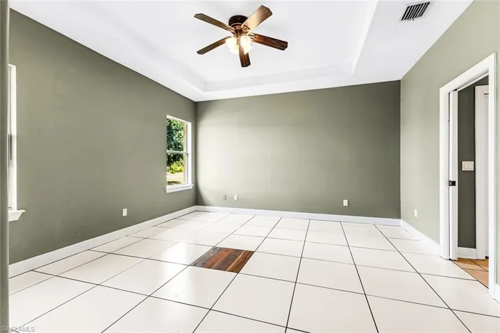 Tiled empty room with ceiling fan, a tray ceiling, and baseboards