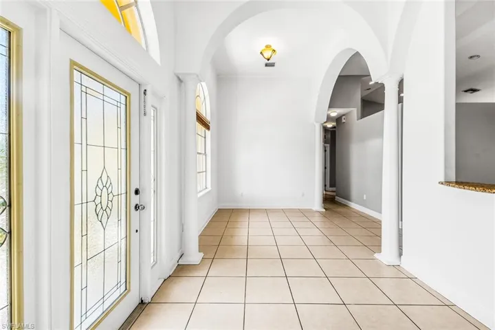 Foyer entrance featuring arched walkways, light tile patterned floors, ornate columns, and baseboards