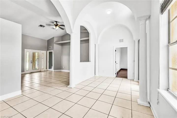 Unfurnished room with ceiling fan, high vaulted ceiling, light tile patterned floors, baseboards, and decorative columns