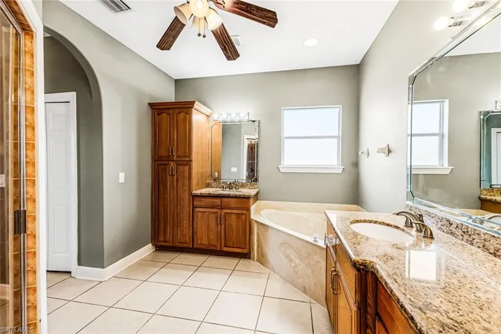Full bathroom featuring ceiling fan, tile patterned floors, a garden tub, two vanities, and baseboards
