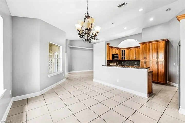 Kitchen with stainless steel microwave, a chandelier, glass insert cabinets, brown cabinets, and backsplash