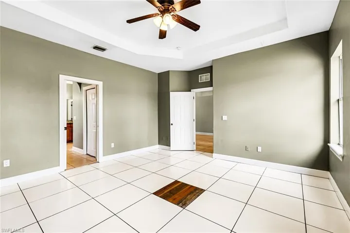 Unfurnished bedroom with a tray ceiling, light tile patterned floors, baseboards, and a ceiling fan