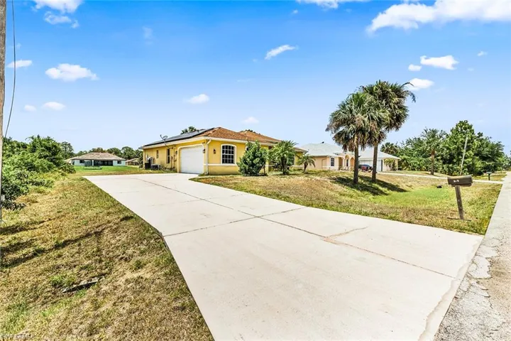 Ranch-style house featuring concrete driveway, solar panels, an attached garage, a front lawn, and stucco siding
