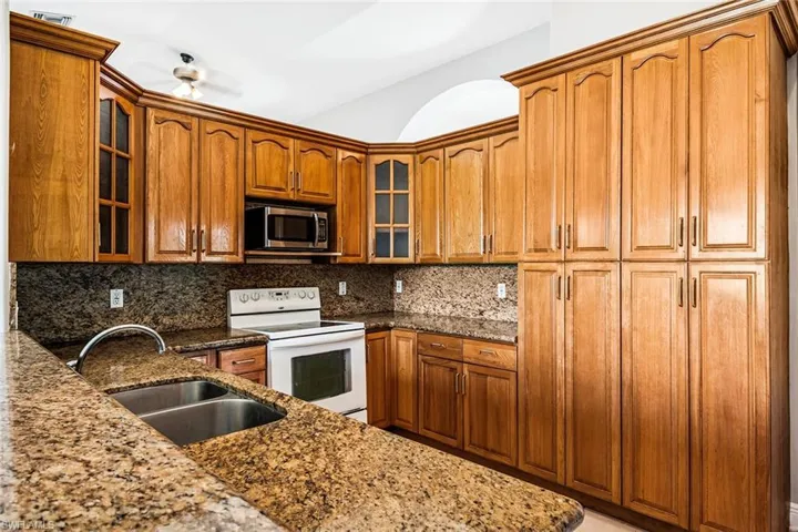 Kitchen with electric range, stainless steel microwave, a sink, stone countertops, and decorative backsplash