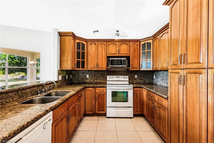 Kitchen with white appliances, a sink, light tile patterned floors, brown cabinetry, and dark stone counters
