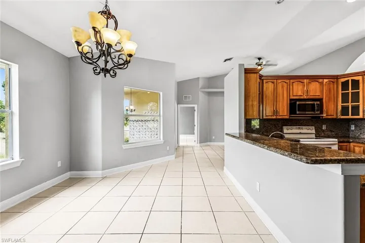 Kitchen featuring white range with electric stovetop, stainless steel microwave, brown cabinetry, decorative backsplash, and glass insert cabinets