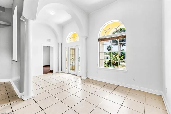 Foyer entrance with plenty of natural light, ornate columns, light tile patterned flooring, a high ceiling, and baseboards