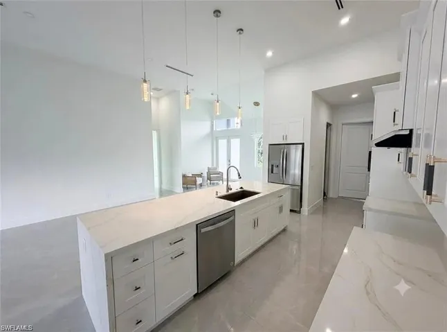 Expansive kitchen featuring a large island with sink, white shaker cabinetry, stainless steel appliances, and sleek pendant lighting