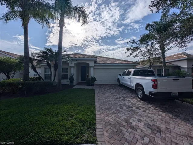 Mediterranean / spanish-style home with an attached garage, decorative driveway, a tiled roof, stucco siding, and a front lawn