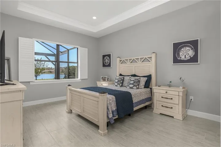 spacious primary bedroom features amazing lake views, tray ceiling with decorative crown molding, plantation shutters, and ensuite spa-like bath.