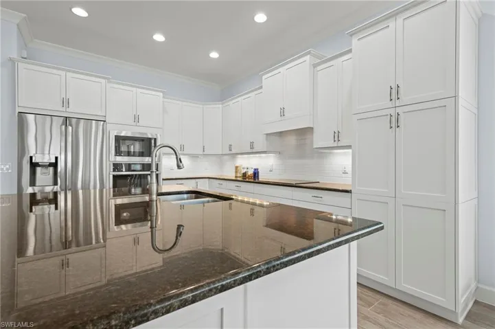Kitchen with dark stone countertops, white cabinetry, and appliances with stainless steel finishes