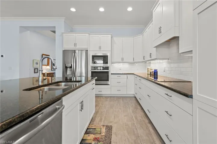 Kitchen with appliances with stainless steel finishes, white cabinetry, sink, dark stone countertops, and ornamental molding