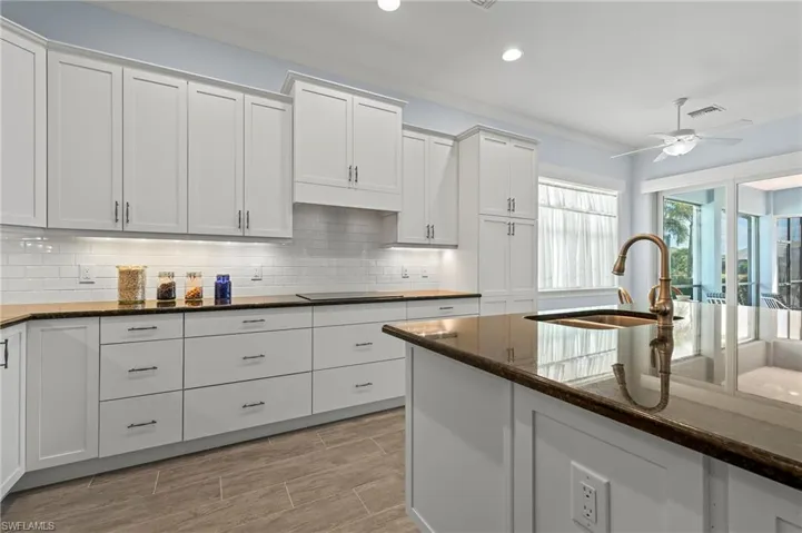 Kitchen with sink, dark stone countertops, white cabinets, ceiling fan, and backsplash