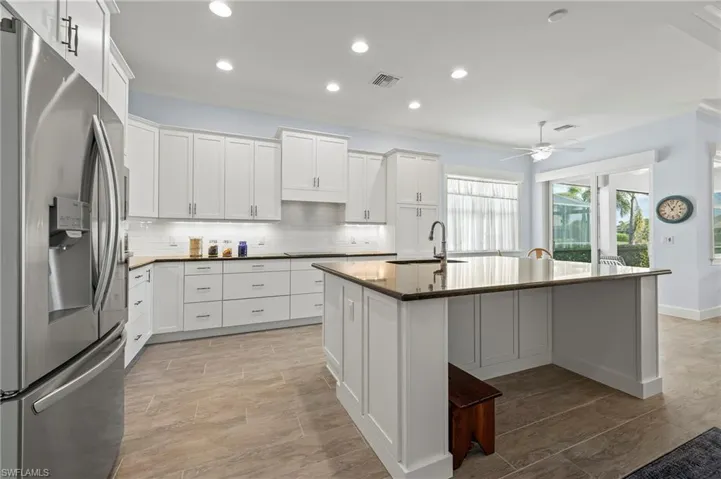 Kitchen with sink, white cabinetry, stainless steel fridge with ice dispenser, a center island with sink, and backsplash