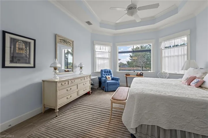 Bedroom with dark wood-type flooring, ornamental molding, a raised ceiling, and ceiling fan