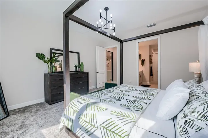 Bedroom featuring ensuite bath, light carpet, and an inviting chandelier