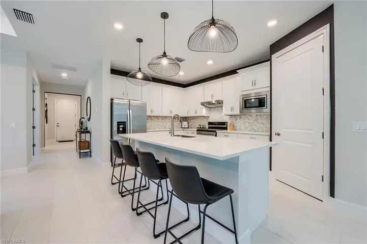 Kitchen with stainless steel appliances, white cabinetry, a kitchen island with sink, and sink