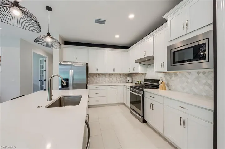 Kitchen featuring appliances with stainless steel finishes, tasteful backsplash, sink, pendant lighting, and white cabinetry