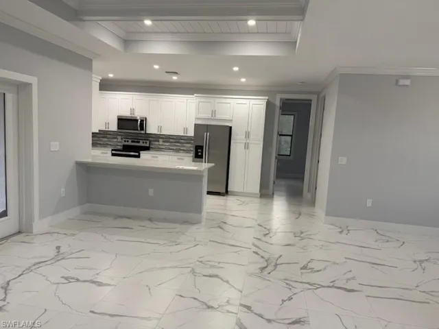Kitchen with stainless steel appliances, backsplash, kitchen peninsula, a tray ceiling, and white cabinets