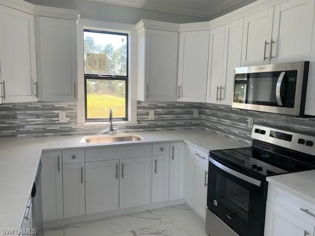 Kitchen with light stone counters, stainless steel appliances, sink, and white cabinets
