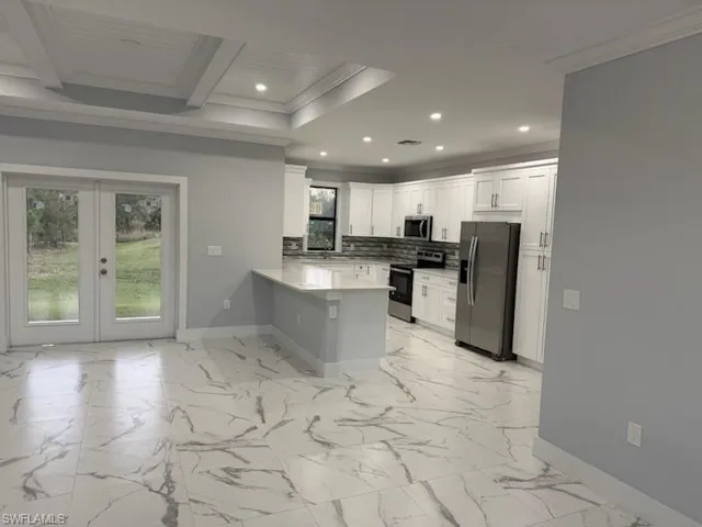 Kitchen featuring french doors, crown molding, white cabinetry, kitchen peninsula, and stainless steel appliances