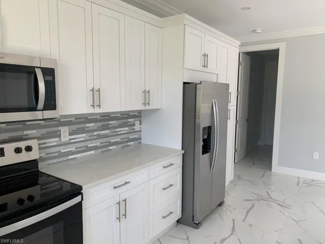 Kitchen featuring appliances with stainless steel finishes, white cabinetry, tasteful backsplash, and light stone counters