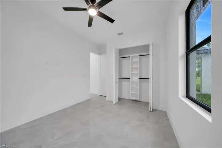 Unfurnished bedroom with multiple windows, a ceiling fan, light marble finish flooring, and a closet