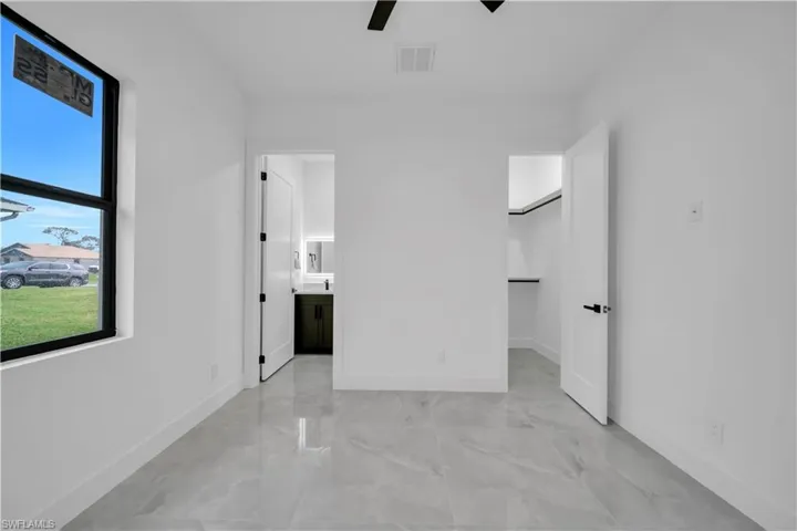 Unfurnished bedroom featuring light marble finish floors, ensuite bath, a walk in closet, and ceiling fan