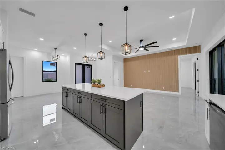 Kitchen with stainless steel appliances, light marble finish floors, a ceiling fan, light countertops, and a kitchen island