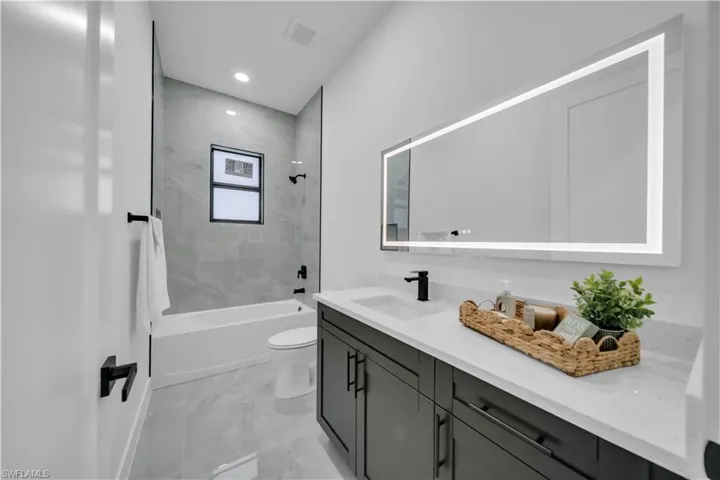 Full bath with vanity, marble finish floors, washtub / shower combination, and recessed lighting
