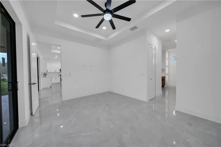 Empty room with a ceiling fan, recessed lighting, light marble finish floors, and a tray ceiling