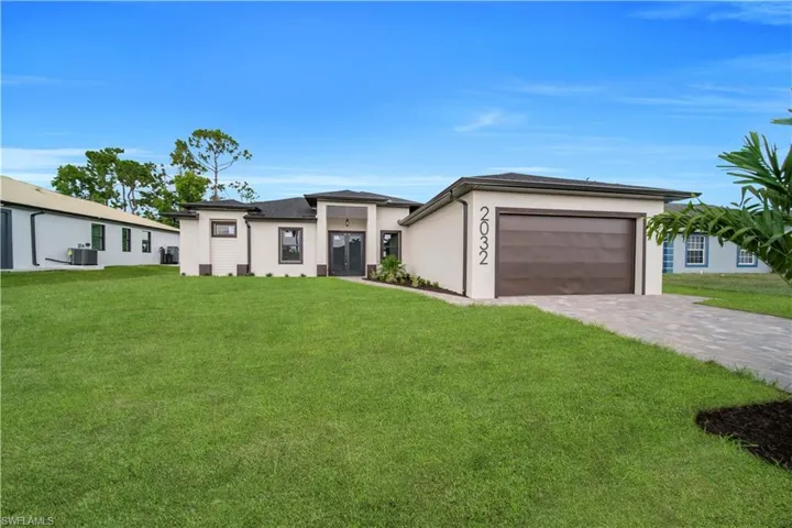 View of front of home with concrete driveway, a lawn, stucco siding, and a detached garage