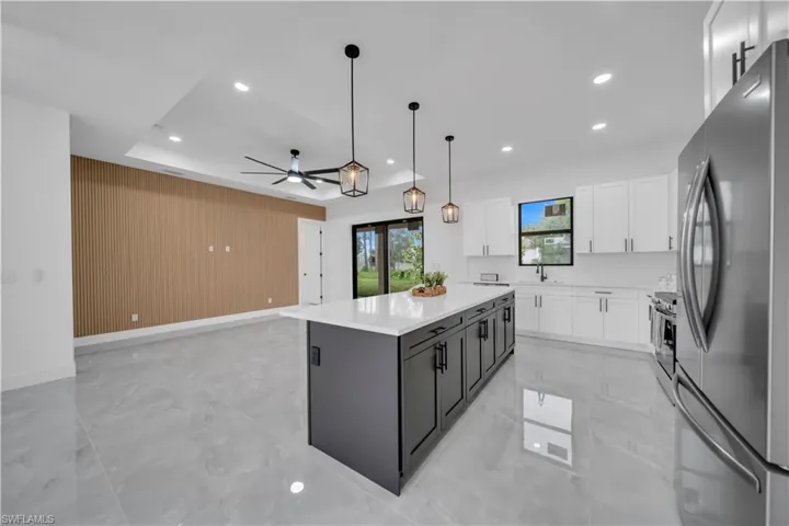 Kitchen with freestanding refrigerator, light marble finish floors, white cabinetry, a kitchen island, and recessed lighting
