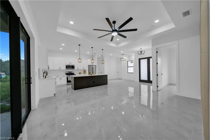 Unfurnished living room with a raised ceiling, recessed lighting, a ceiling fan, and light marble finish flooring