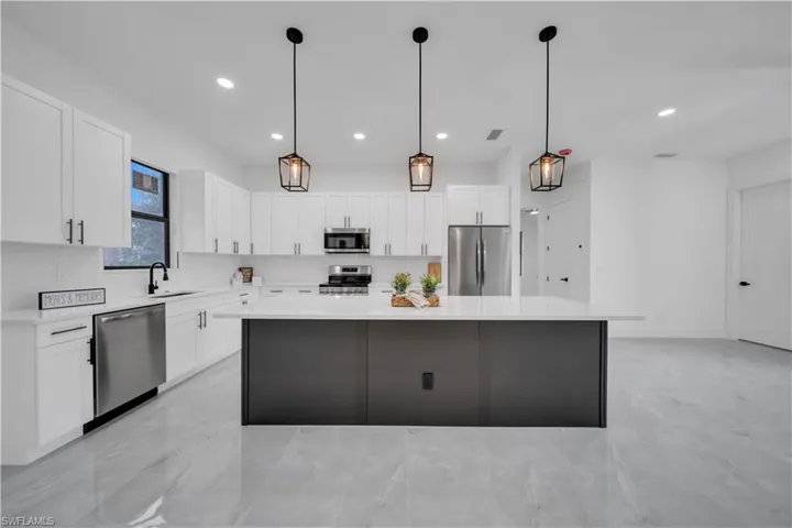 Kitchen with stainless steel appliances, light marble finish floors, a kitchen island, white cabinetry, and recessed lighting