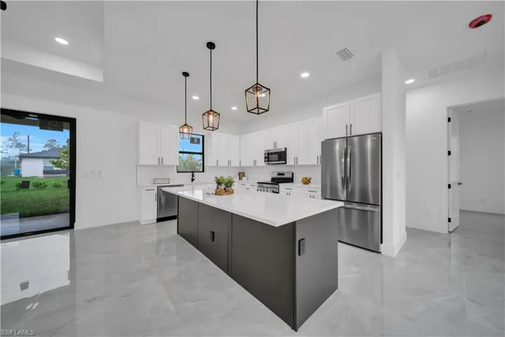 Kitchen with stainless steel appliances, light marble finish floors, a kitchen island, recessed lighting, and white cabinets