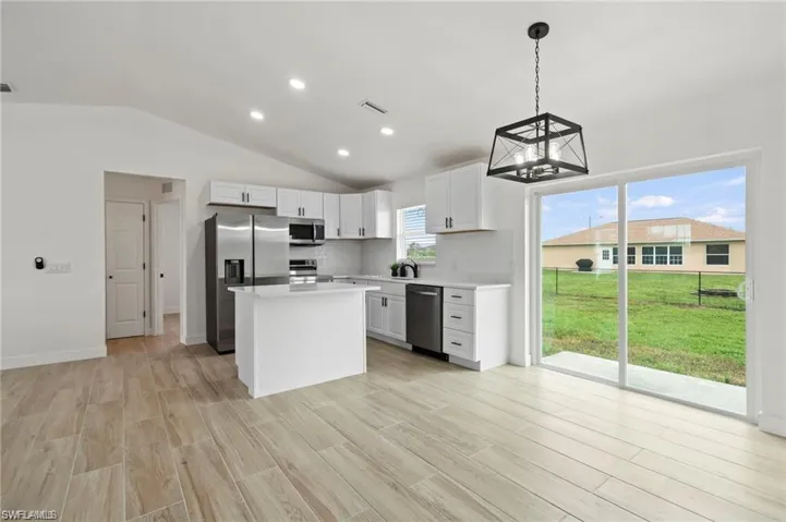 Kitchen featuring vaulted ceiling, decorative light fixtures, stainless steel appliances, light hardwood / wood-style floors, and white cabinetry