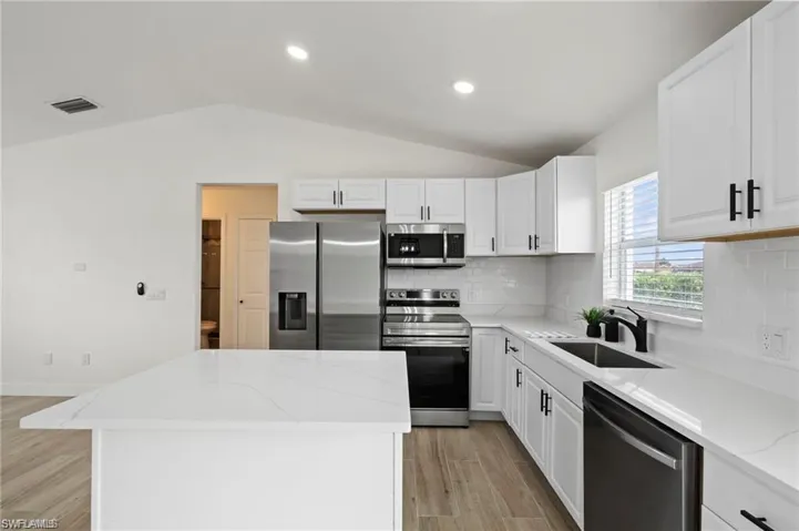 Kitchen featuring a kitchen island, stainless steel appliances, white cabinetry, and vaulted ceiling