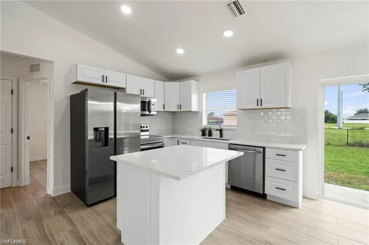 Kitchen featuring a kitchen island, vaulted ceiling, appliances with stainless steel finishes, light wood-type flooring, and white cabinets