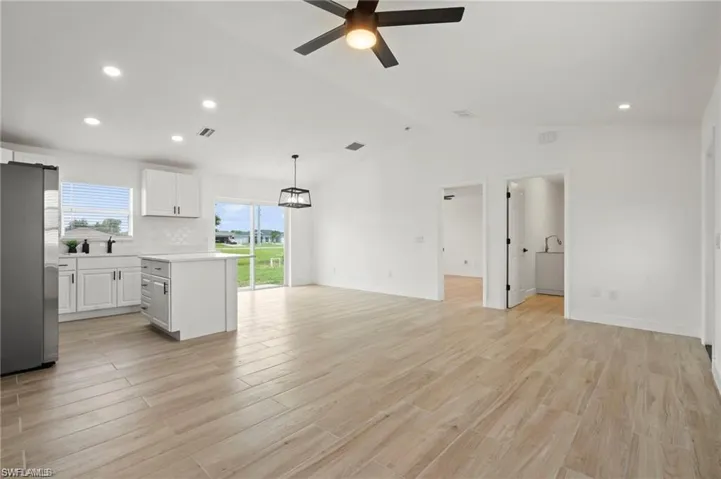 Kitchen featuring vaulted ceiling, light hardwood / wood-style flooring, stainless steel refrigerator, white cabinetry, and ceiling fan